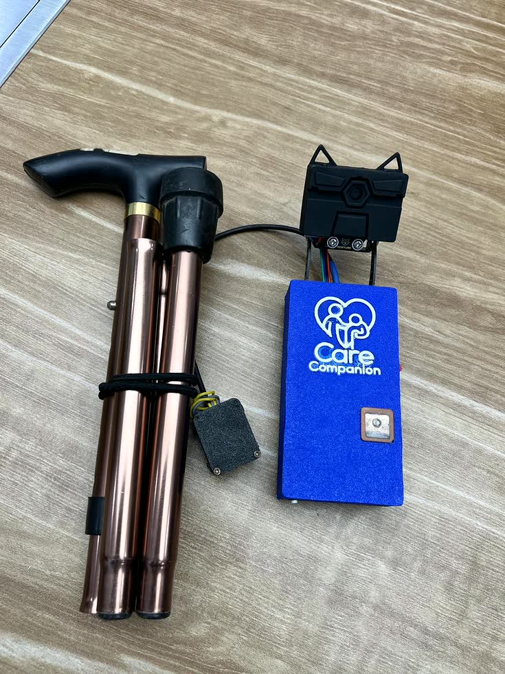 The walking cane folded down into four sections on a desk, with the CareCompanion enclosure, its camera and the display module lying detached beside it.